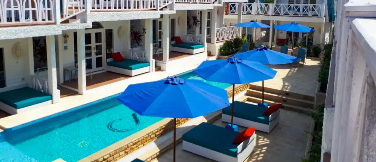 Relaxing resort courtyard with white buildings, a long pool, and blue umbrellas on Gili Trawangan.