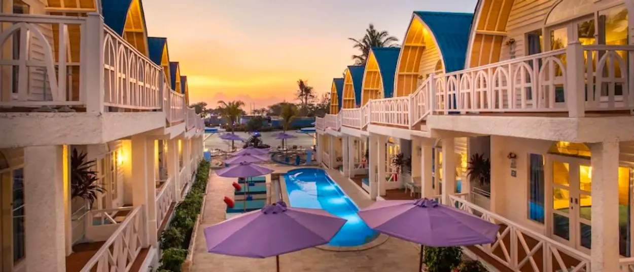 White bungalows with blue roofs line a swimming pool at sunset in Gili Trawangan.
