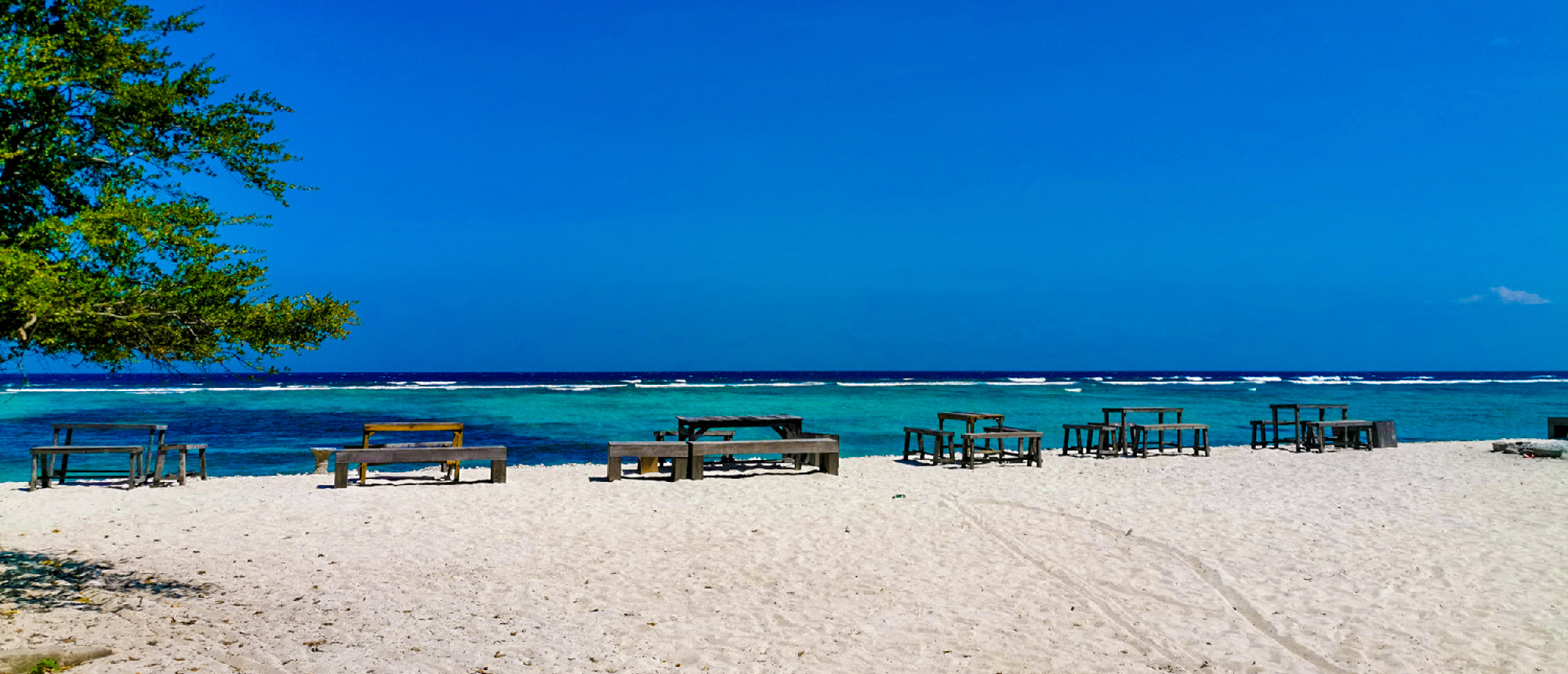 Idyllic Gili Trawangan beach with white sand, wooden seating, and clear turquoise water.