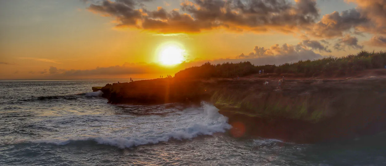 Golden sunset over the ocean, with waves crashing against the rocky Nusa Lembongan coastline.