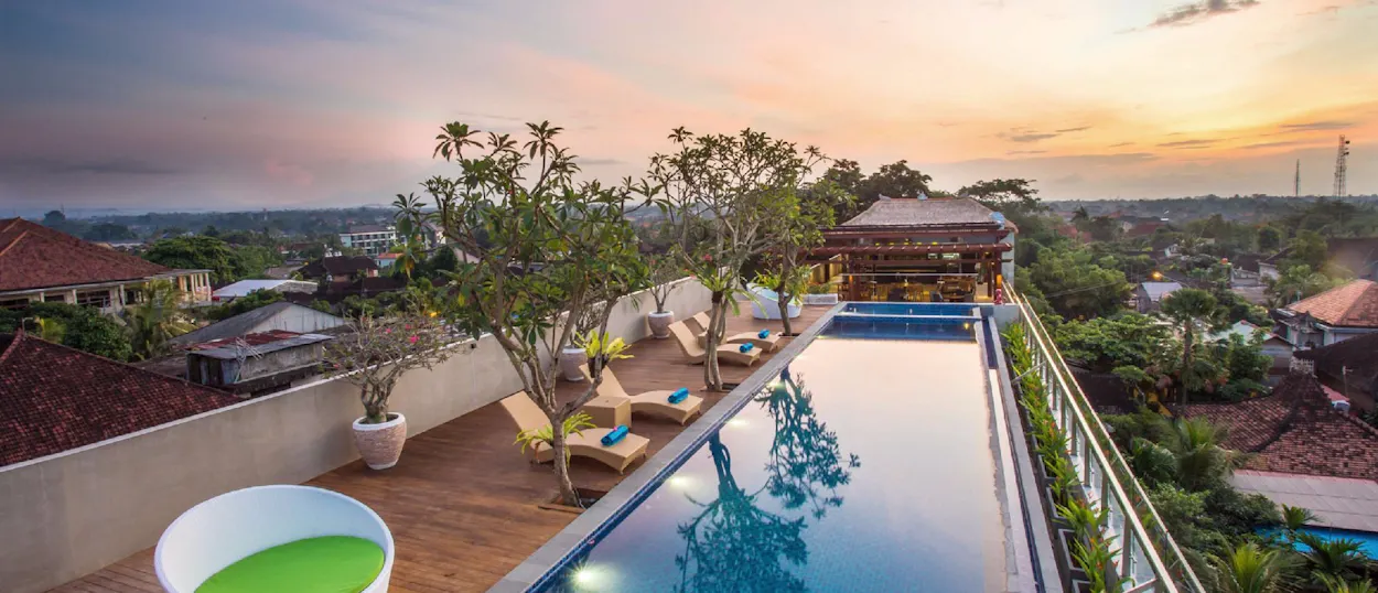 Rooftop infinity pool overlooking Ubud at sunset, with lounge chairs and lush trees.