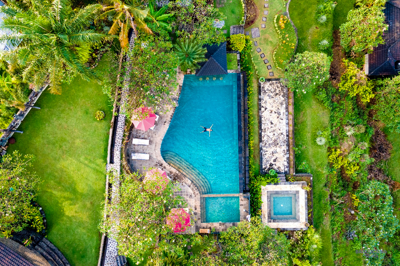 A person floats in a serene blue swimming pool at a tropical resort in Lovina, Bali.