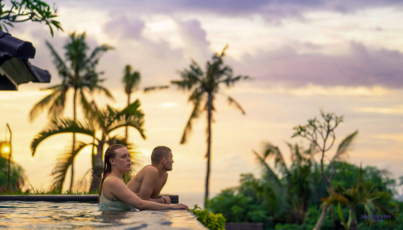 A couple watches a vibrant sunset from an infinity pool overlooking Lovina, Bali.