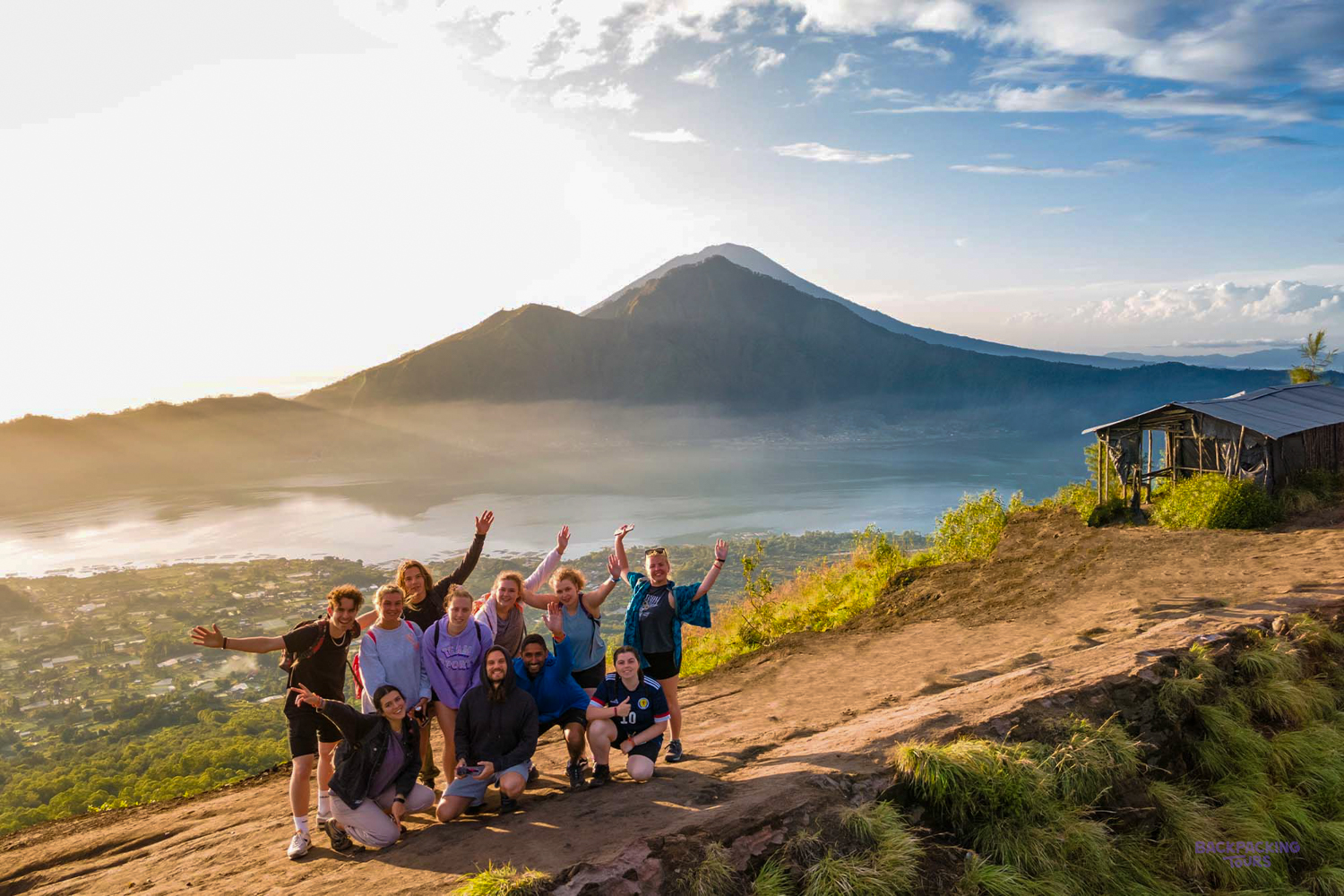 A joyful group of backpackers waving at sunrise on Mount Batur, overlooking Lake Batur.