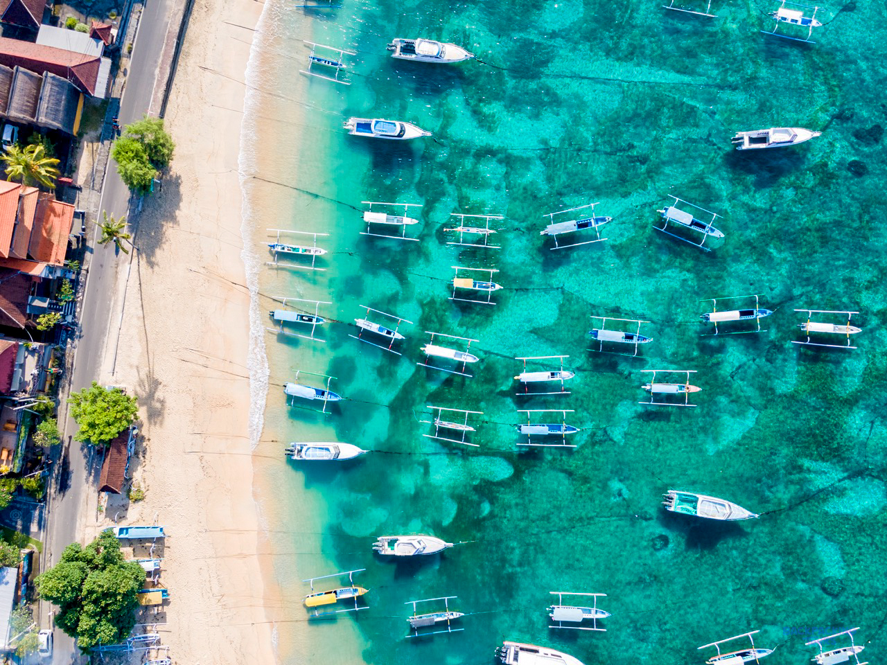 Many traditional outrigger boats rest on the clear turquoise waters of a Balinese beach.