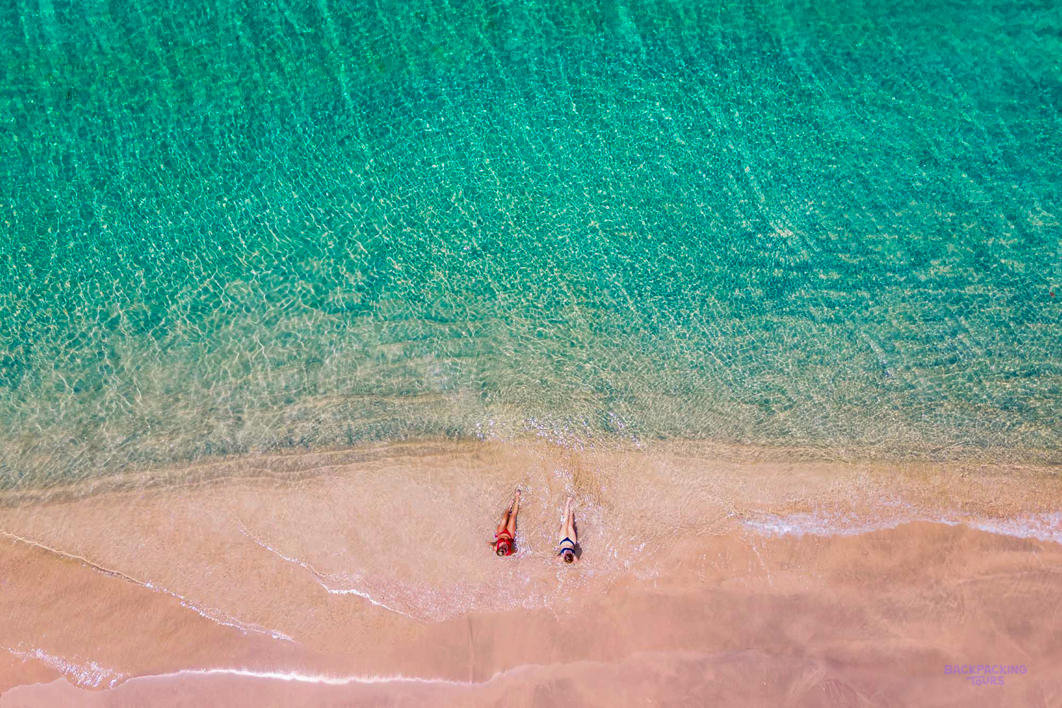 Two people relax on a pristine sandy beach with crystal-clear turquoise water in the Gili Islands.