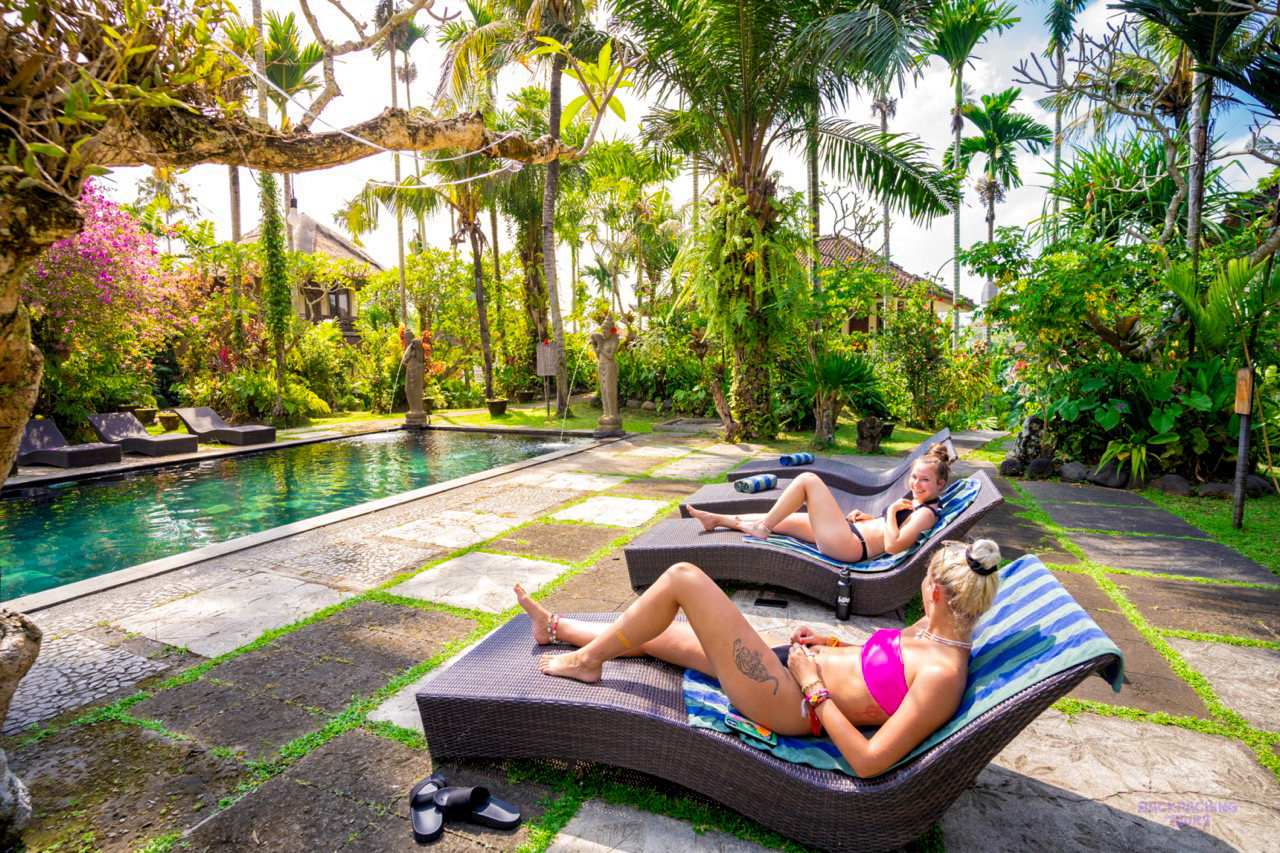 Two women relaxing by a beautiful swimming pool surrounded by lush tropical plants in Ubud, Bali.