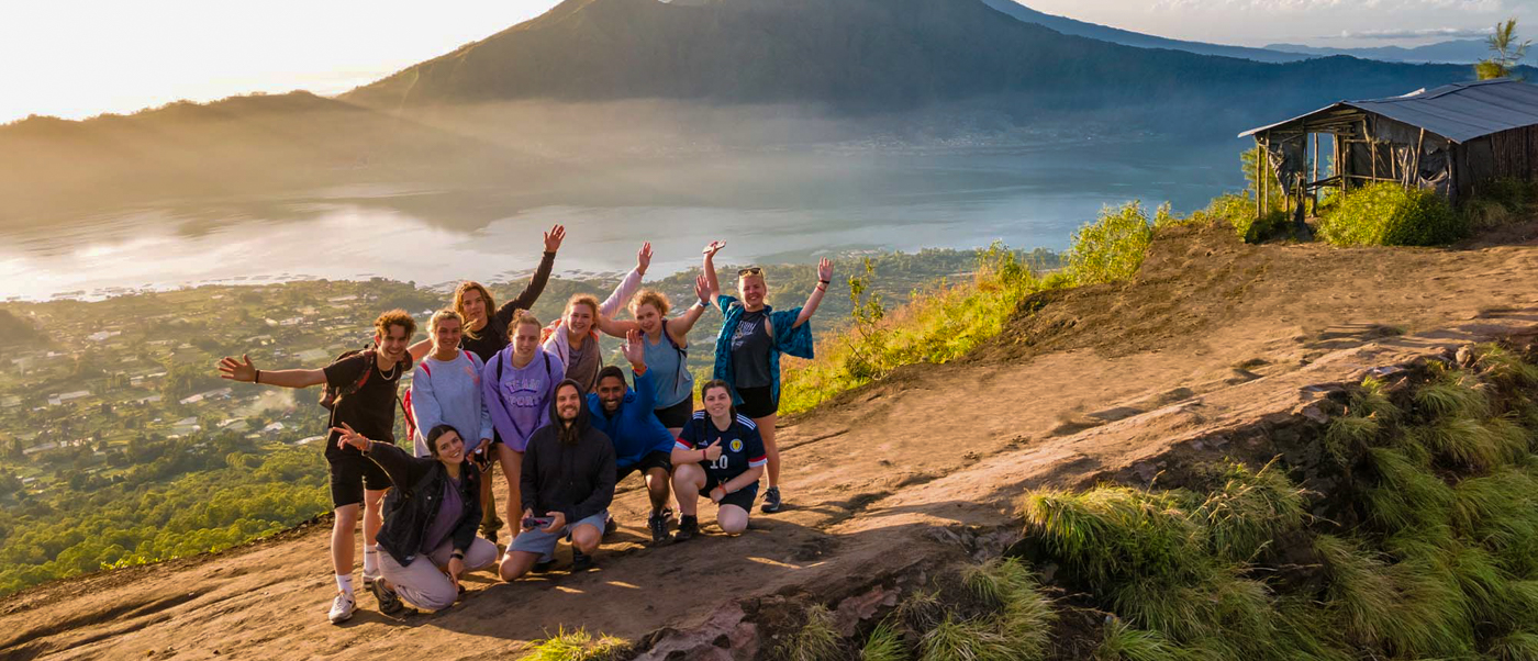 A joyful group of friends pose on Mount Batur at sunrise, celebrating panoramic views across Bali.