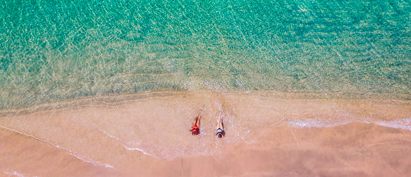 Two people relax on a pristine sandy beach with clear turquoise water in the Gili Islands.