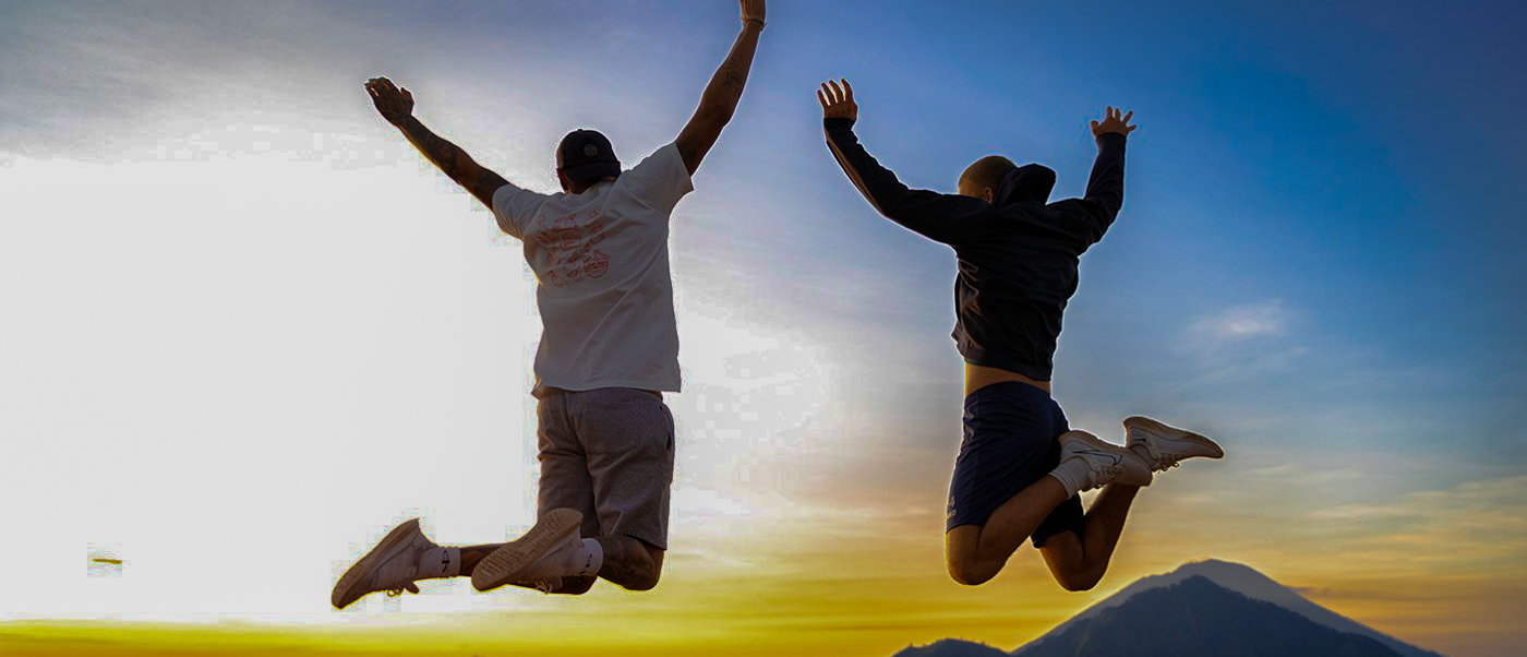 Two excited travelers jump with arms raised against a stunning sunrise over Mount Batur, Bali.