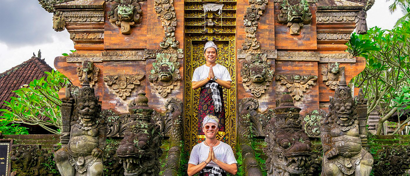 Two men in traditional Balinese attire pose respectfully at an ancient temple gate in Canggu.
