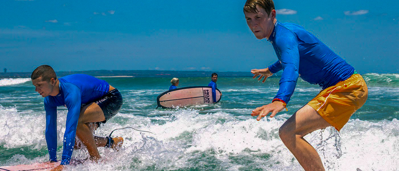 Two young men learn to surf on small waves at a sunny beach in Canggu, Bali.