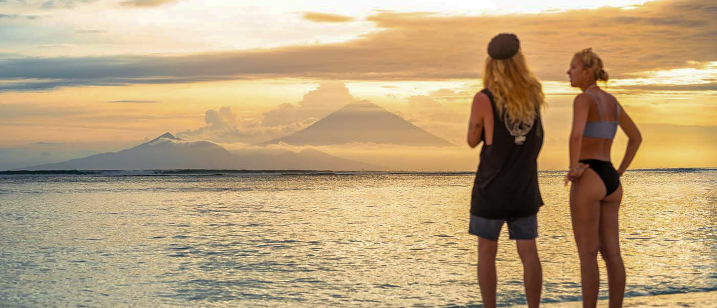 Two people watch a beautiful golden sunset over the calm ocean with distant mountains at Gili Trawangan.