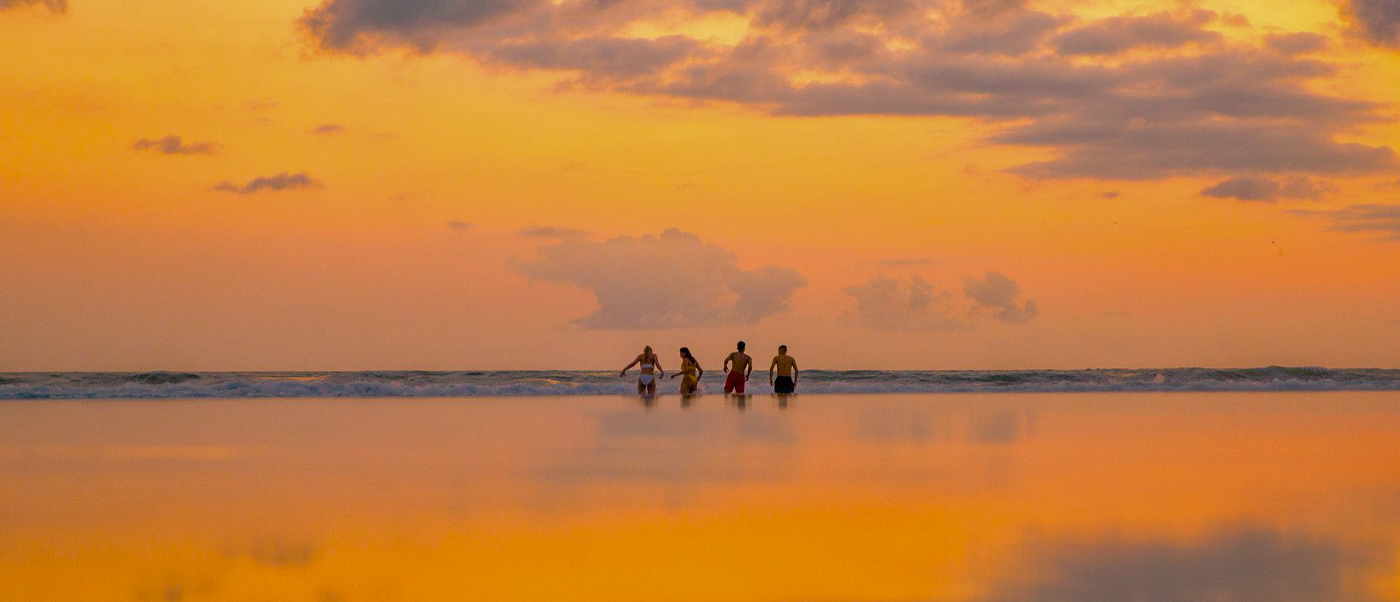 Four friends silhouetted against a vibrant orange sunset on the calm waters of Gili Trawangan.