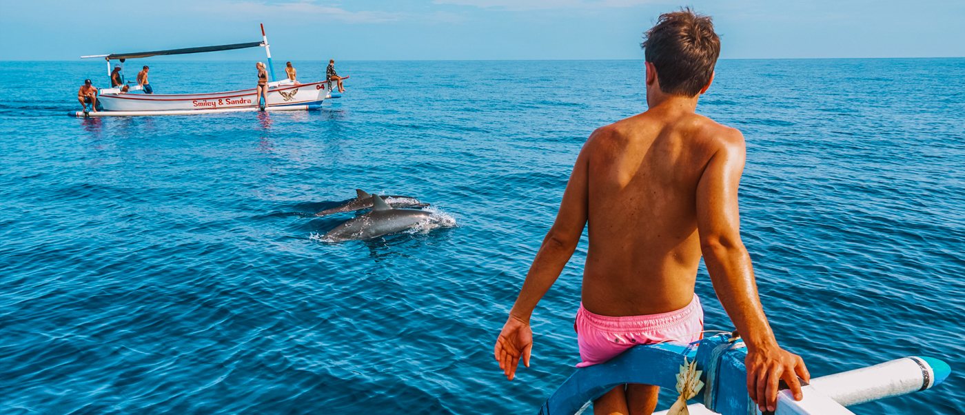 A traveler on a traditional boat watches wild dolphins swim in the blue ocean off Lovina, Bali.