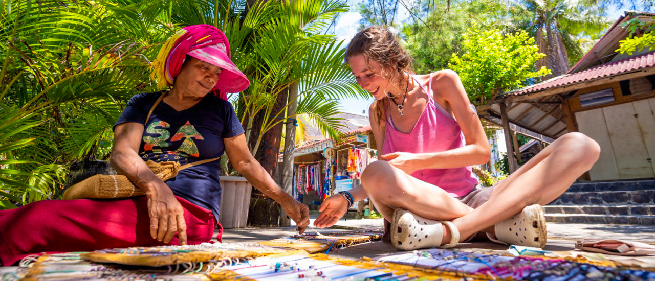 Two women smiling while looking at handmade bracelets at a market stall on Gili Trawangan.