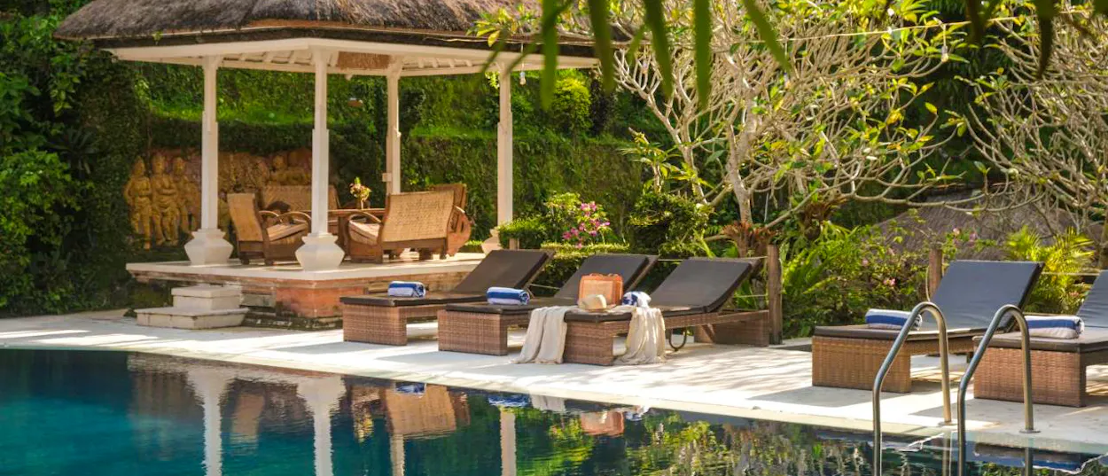 Relaxing poolside scene with comfortable lounge chairs and a beautiful traditional gazebo in Ubud, Bali.