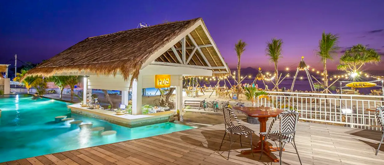 A vibrant swim-up bar with a thatched roof at a beachside resort on Gili Trawangan at sunset.
