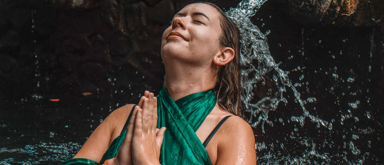 A serene woman with closed eyes performs a purification ritual under flowing water in Ubud.