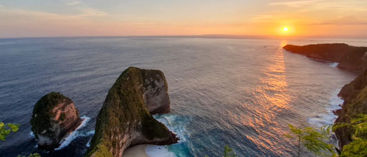 Sunset over the T-Rex shaped Kelingking Beach on Nusa Penida, with golden light on the ocean.