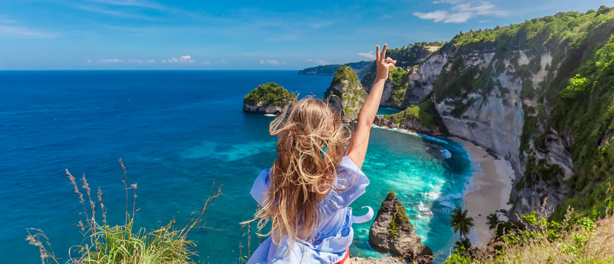 A happy traveler makes a peace sign overlooking the stunning Diamond Beach in Nusa Penida.