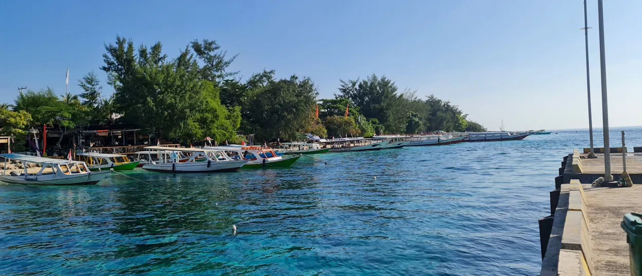 Boats docked along the clear turquoise waters of Pemuteran, Bali, under a sunny sky.