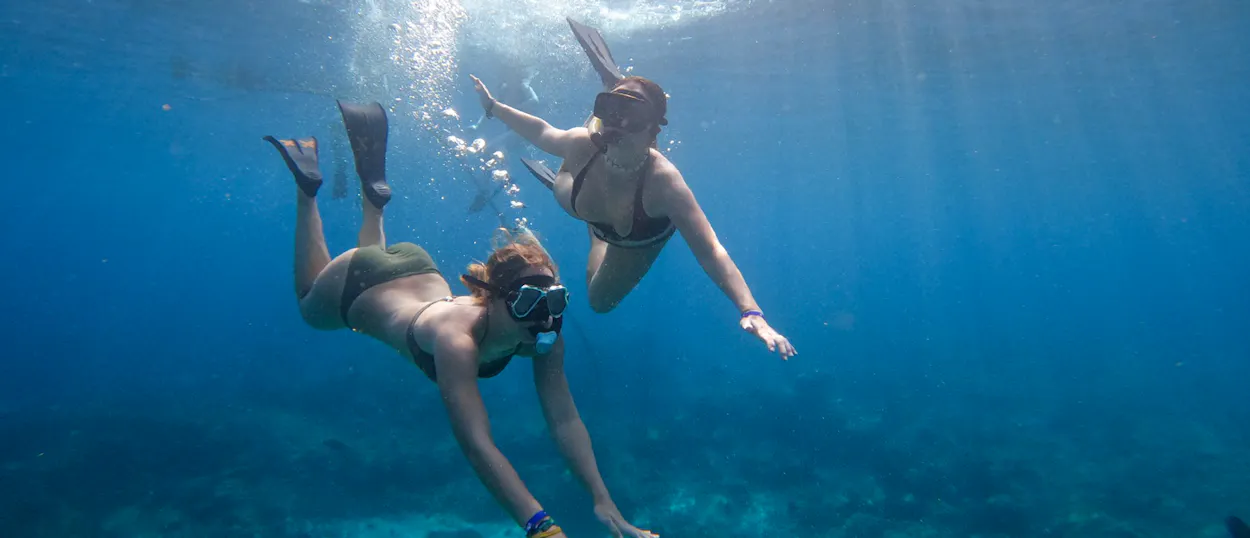 Two women snorkel in clear blue water, exploring vibrant coral reefs in Menjangan Island, Bali.