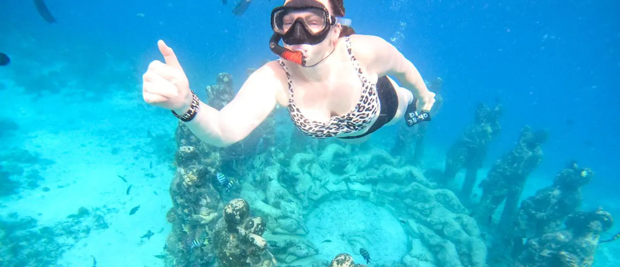 A happy snorkeler gives a thumbs-up underwater among the statues in Gili Trawangan.