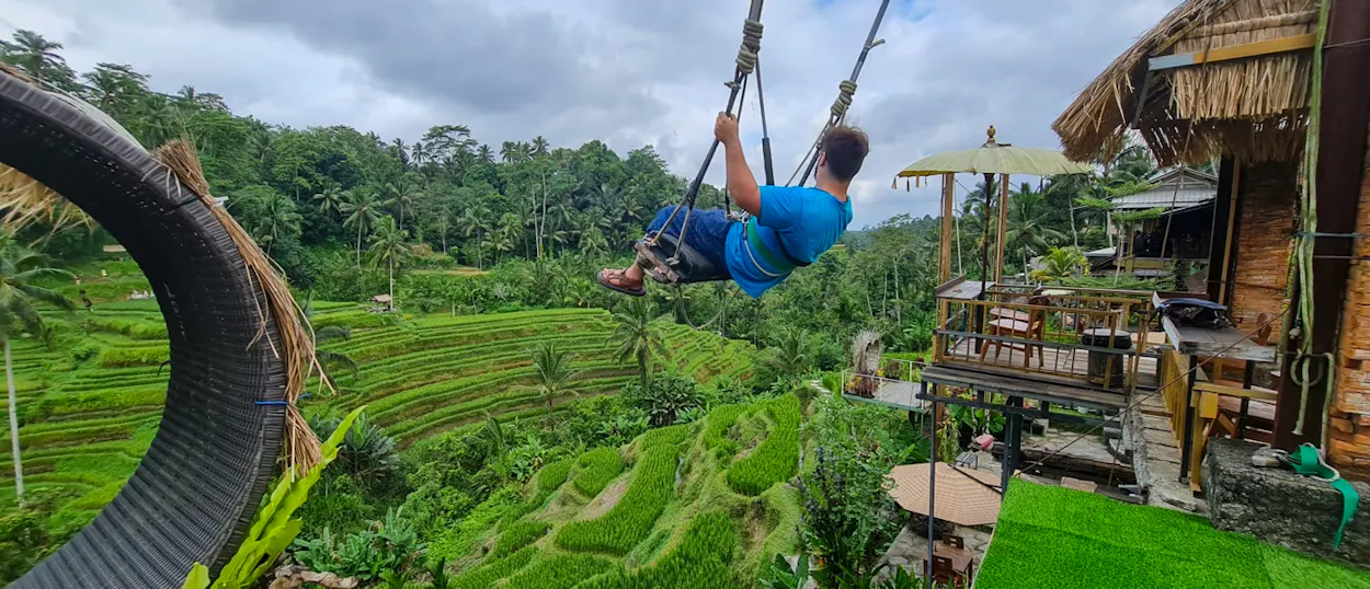 A man on a swing soars high above the vibrant green Tegallalang rice terraces in Bali.