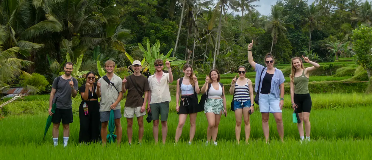 Ten happy backpackers pose in the lush green rice terraces of Ubud, Bali.