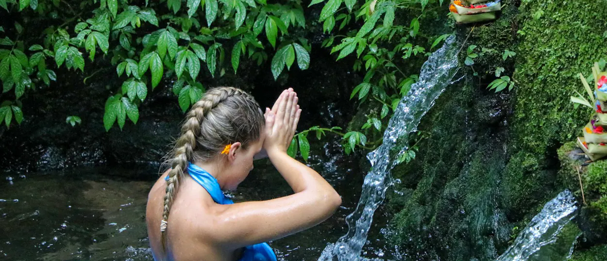A woman performs a purification ritual under flowing water at a sacred temple in Bali.
