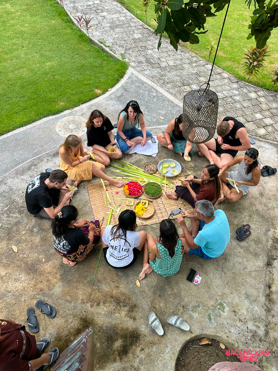 A group of travelers crafting traditional Balinese offerings with colorful flowers and palm leaves in Ubud.