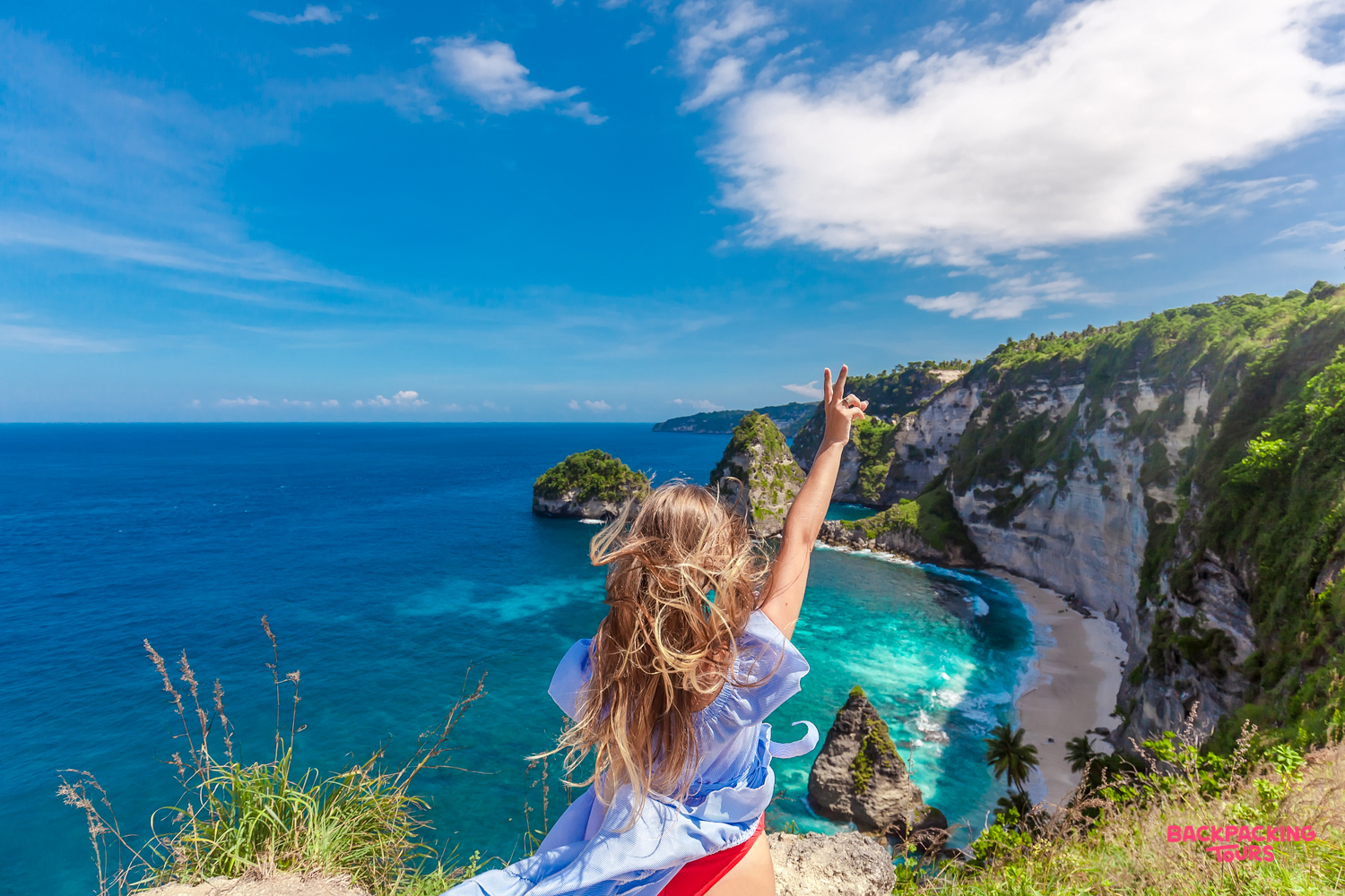 A joyful traveler makes a peace sign overlooking the beautiful Diamond Beach in Nusa Penida.