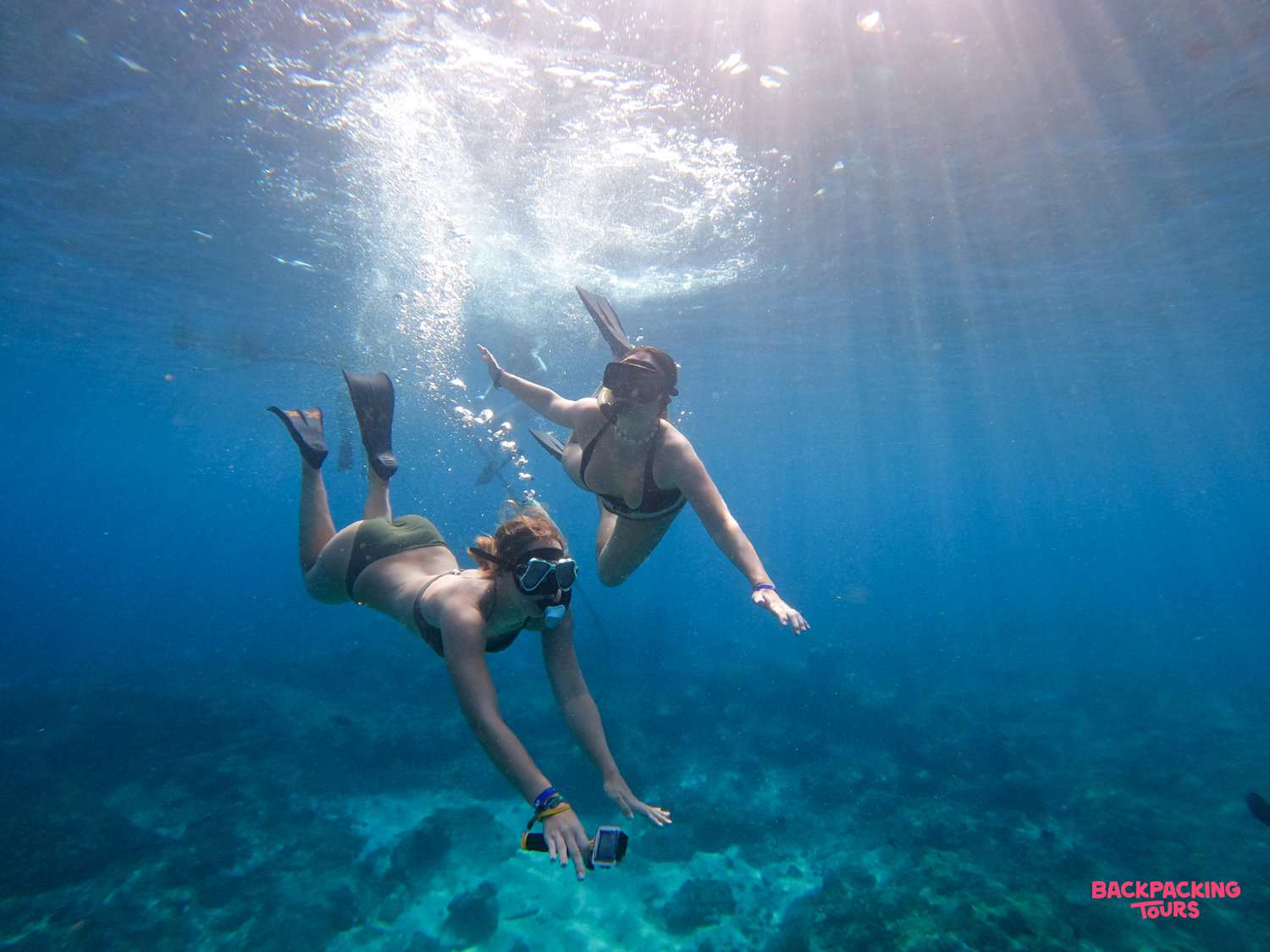 Two women freedive in clear blue waters, exploring the vibrant underwater world near Menjangan Island, Bali.
