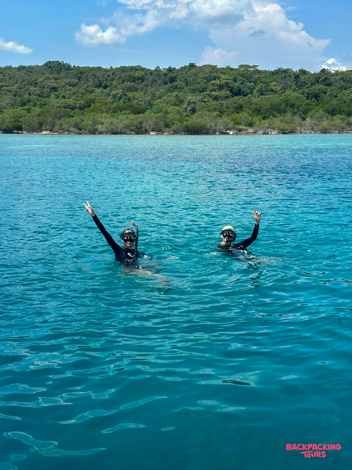 Two happy snorkelers wave from the clear blue waters of Menjangan Island, Bali.