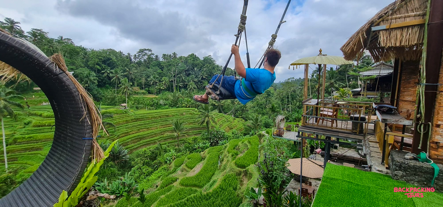 A traveler on a giant swing overlooks the beautiful terraced rice fields of Ubud, Bali.