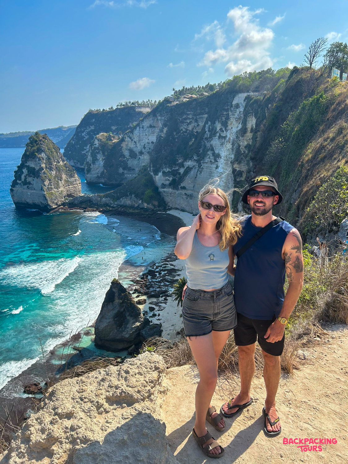 Happy travelers pose at the iconic T-Rex cliff overlooking the turquoise waters of Kelingking Beach, Nusa Penida.