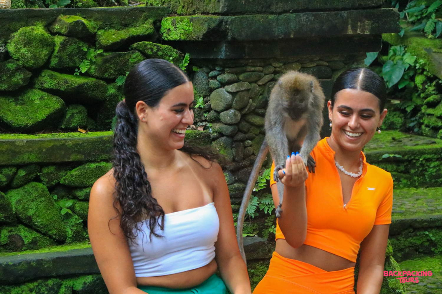 Two friends share a joyful moment with a monkey in the beautiful Ubud Monkey Forest.