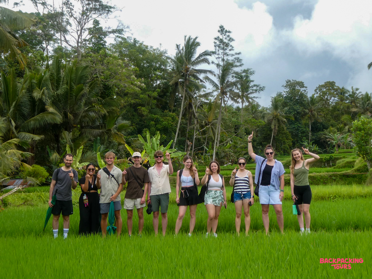 A group of happy backpackers standing in a vibrant green rice field in Ubud, Bali.