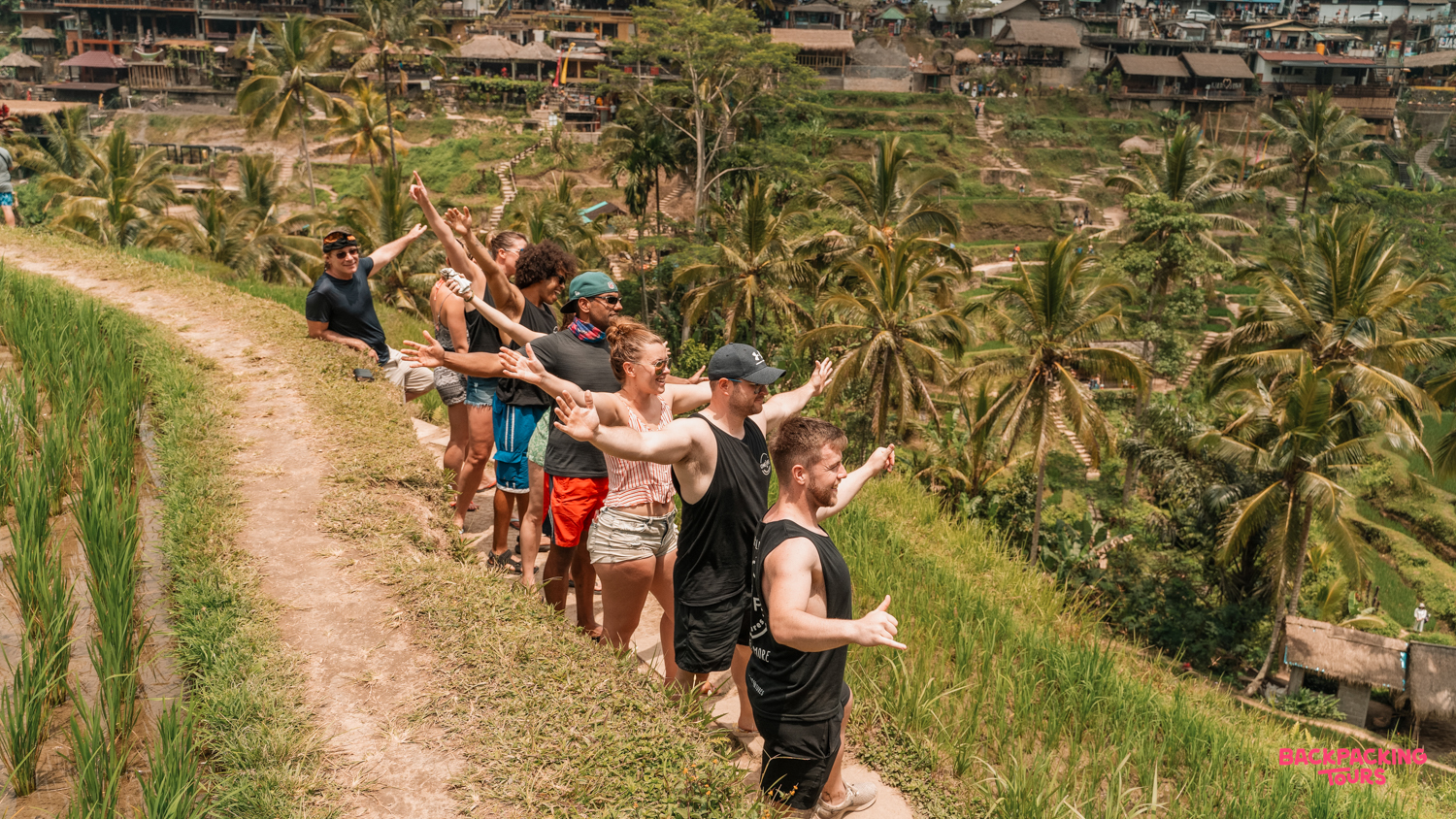 A group of backpackers pose with outstretched arms overlooking the beautiful Tegallalang rice terraces in Ubud, Bali.