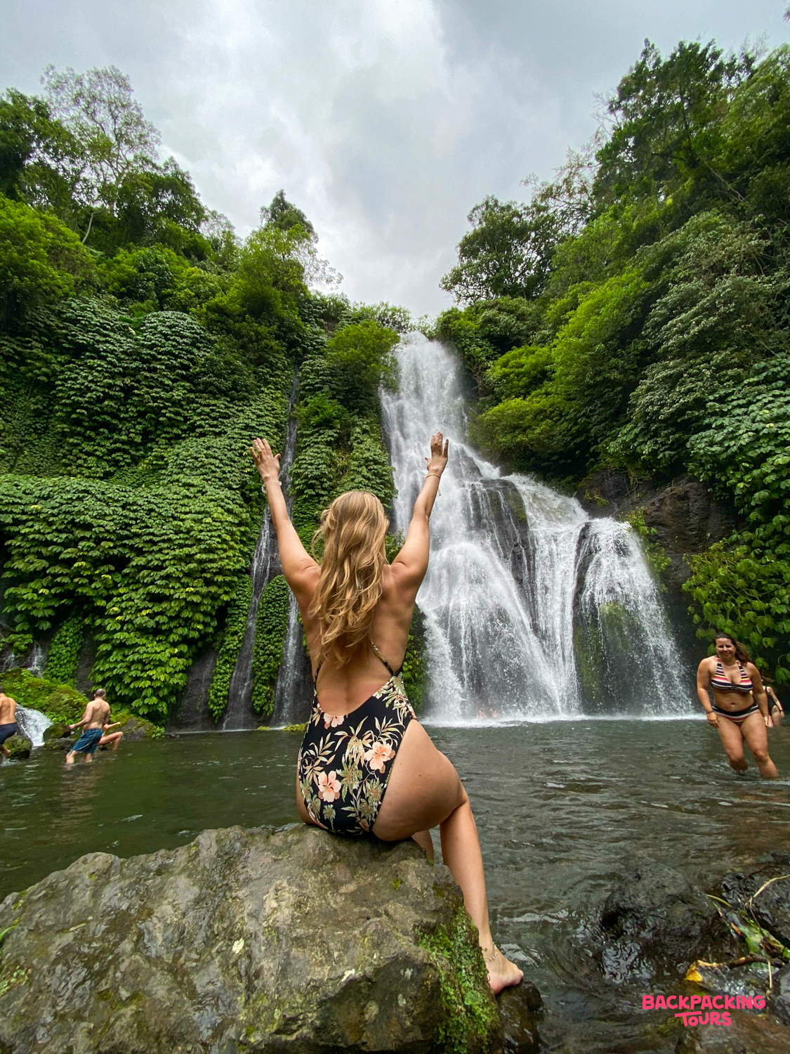 Happy traveler with arms raised enjoying the refreshing waters of a beautiful jungle waterfall in Bali.