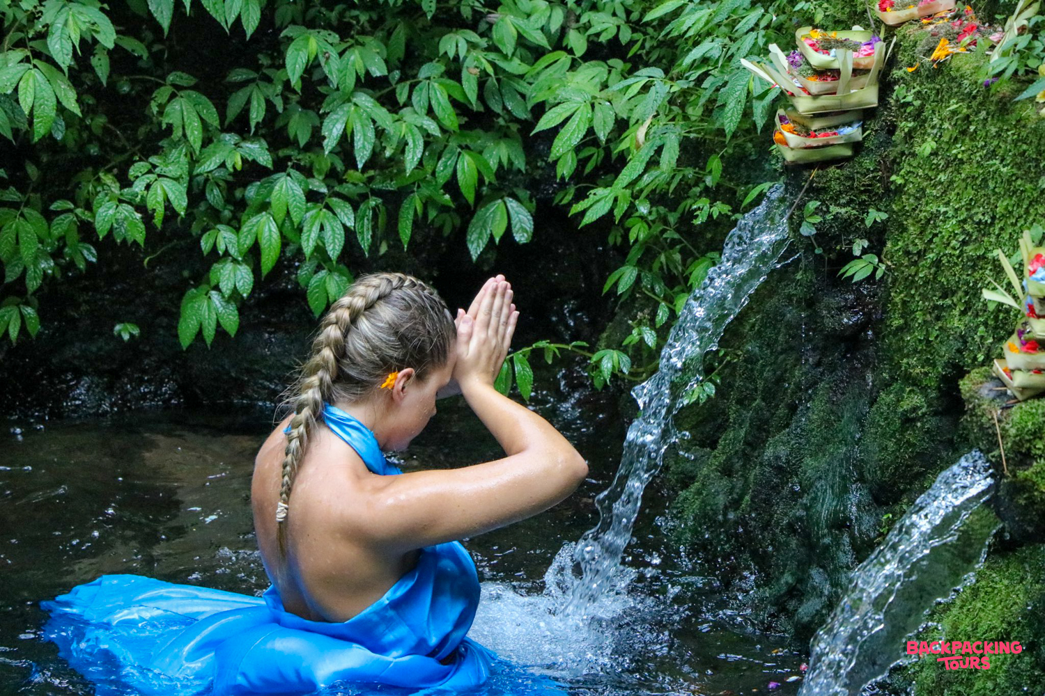 A woman in a blue dress performs a purification ritual in the sacred waters of Tirta Empul temple.