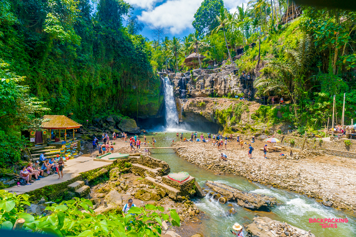 Tourists swim and relax at the base of Tegenungan Waterfall in lush Ubud, Bali.
