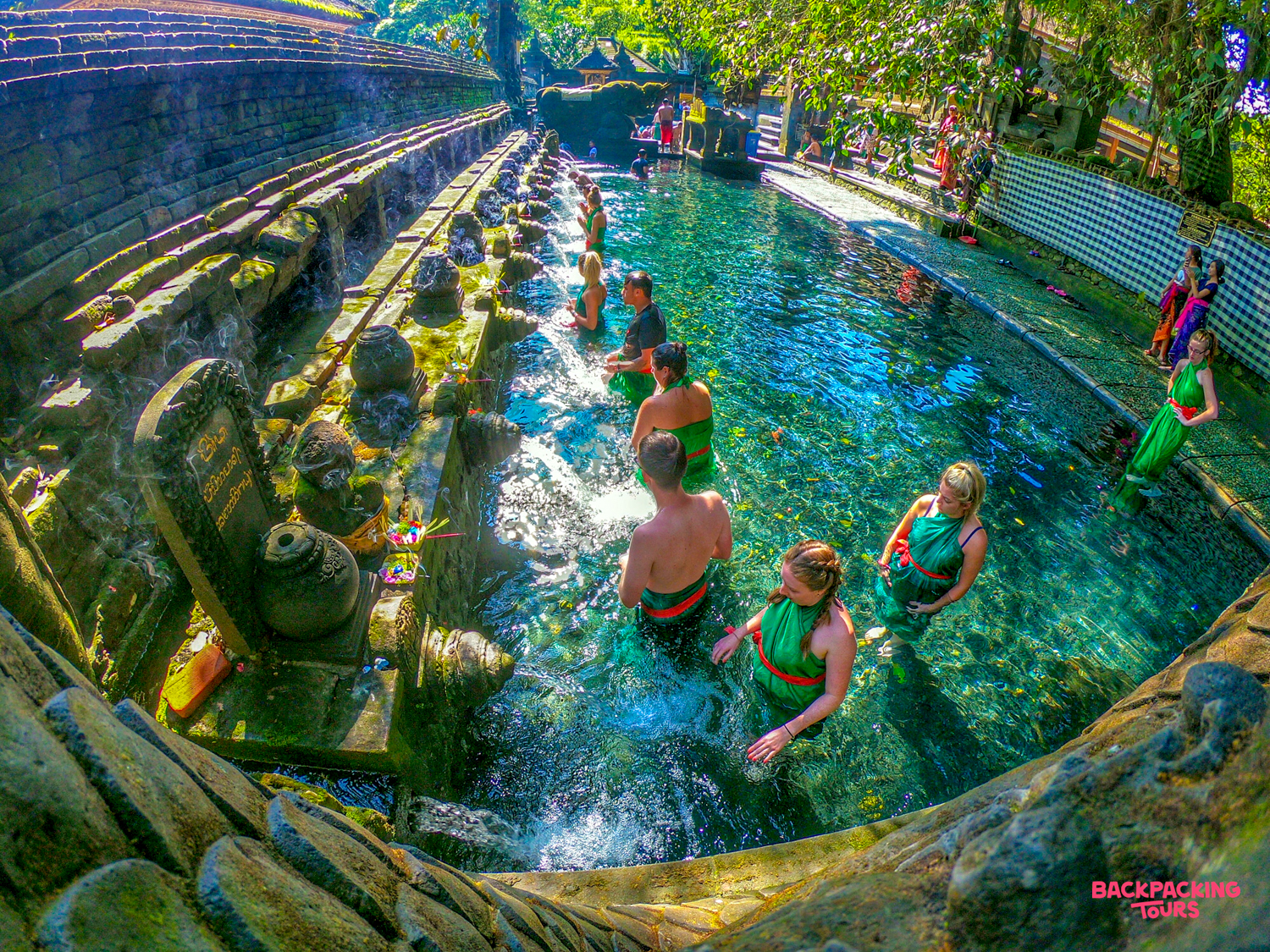 Tourists in green sarongs participate in a traditional water blessing at Tirta Empul temple in Bali.