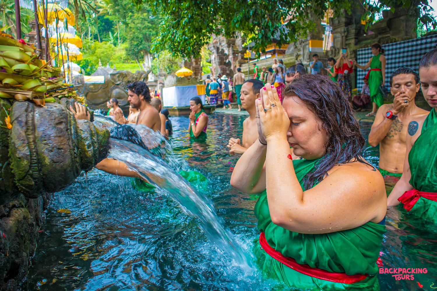 Travelers in green sarongs participate in a traditional water blessing ritual at Tirta Empul temple in Bali.