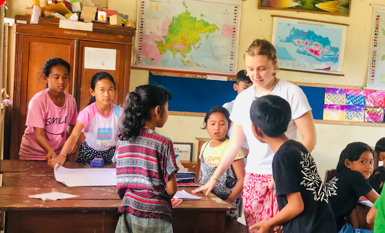 A female volunteer teaches a group of children in a bright classroom in Bali.