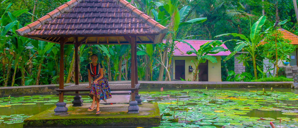 Woman relaxing in a traditional gazebo over a lily pond amidst lush greenery in Ubud, Bali.