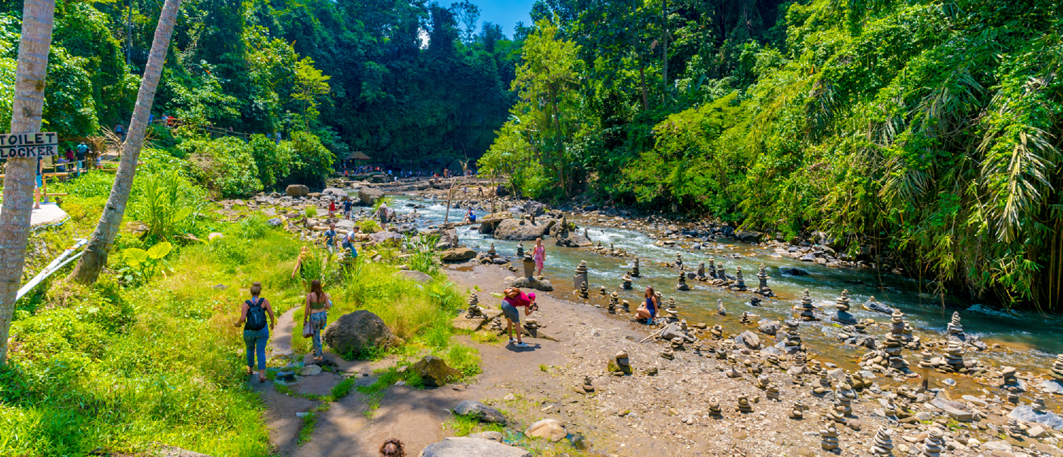 Travelers explore a rocky river with many rock stacks, surrounded by lush green jungle in Ubud.