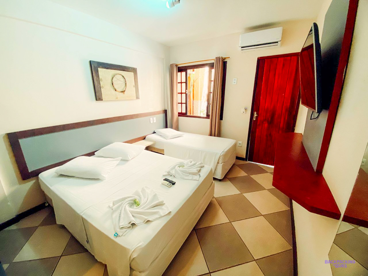 A room with white beds, a red door and a chequered floor at the pousada on Ilha Grande