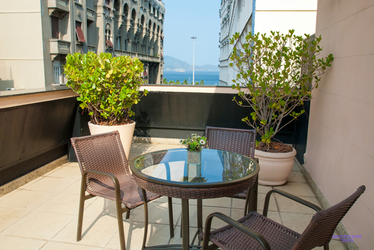 A balcony with a glass table, chairs and potted plants at the hotel in Rio de Janeiro, with a glimpse of the sea